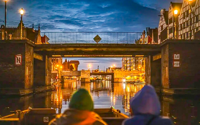 Guests on a historical boat cruise under a bridge in Gdansk at sunset.