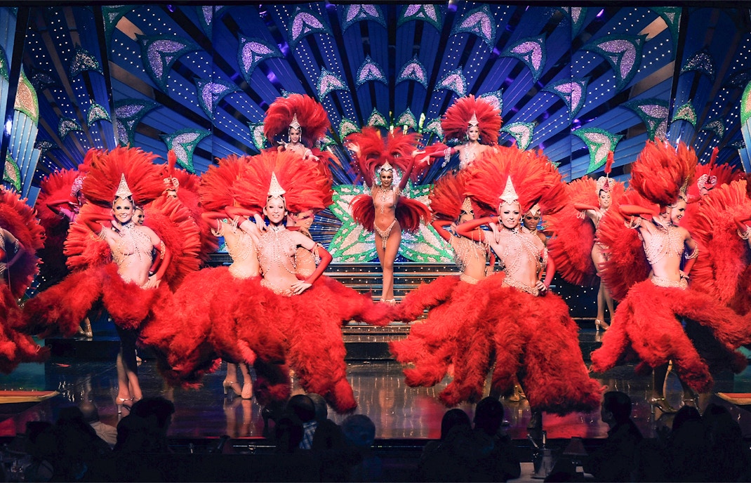 Performers in red feather costumes at Moulin Rouge show, Paris stage.