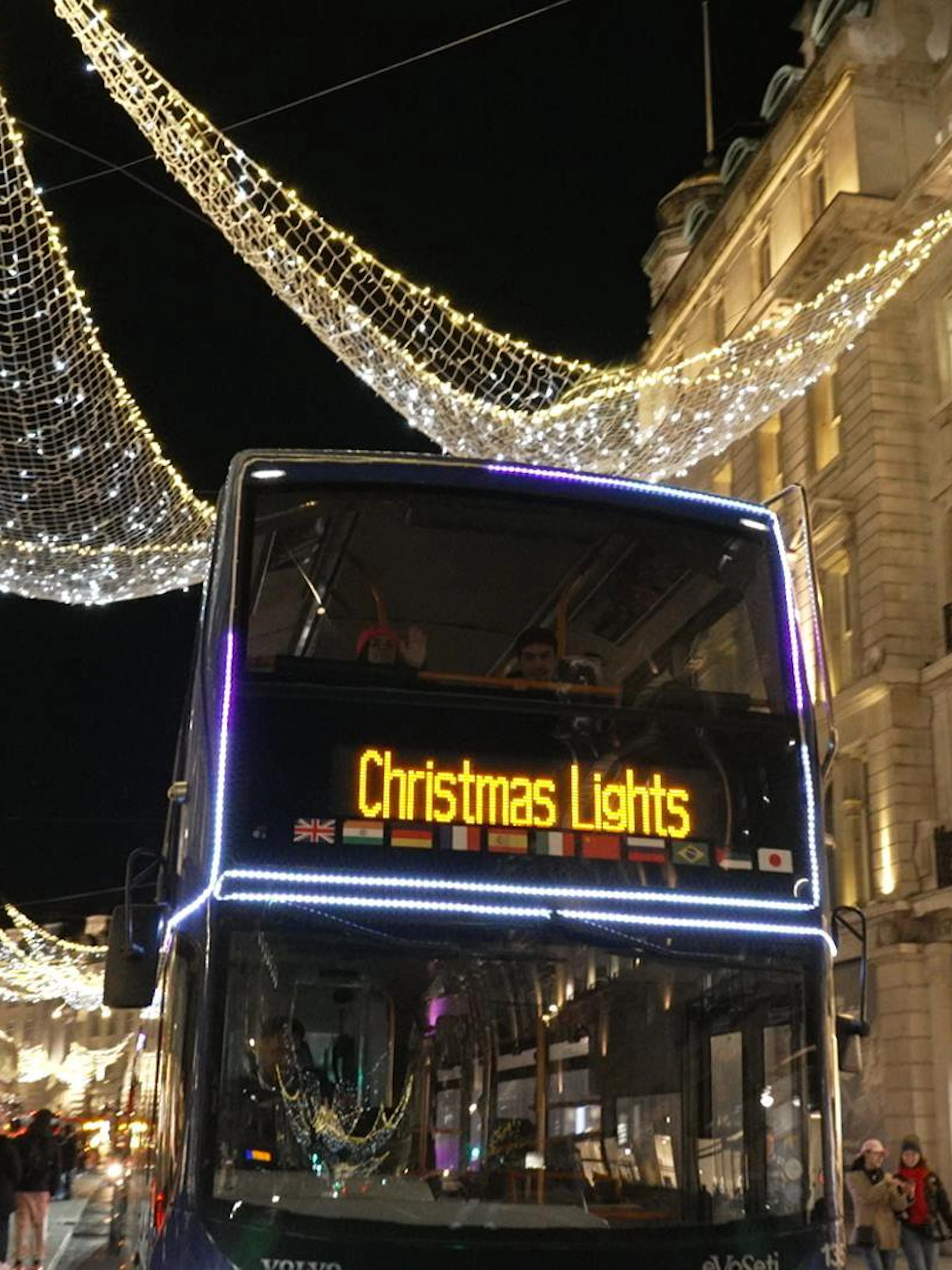 London night bus under Christmas lights on a festive street.