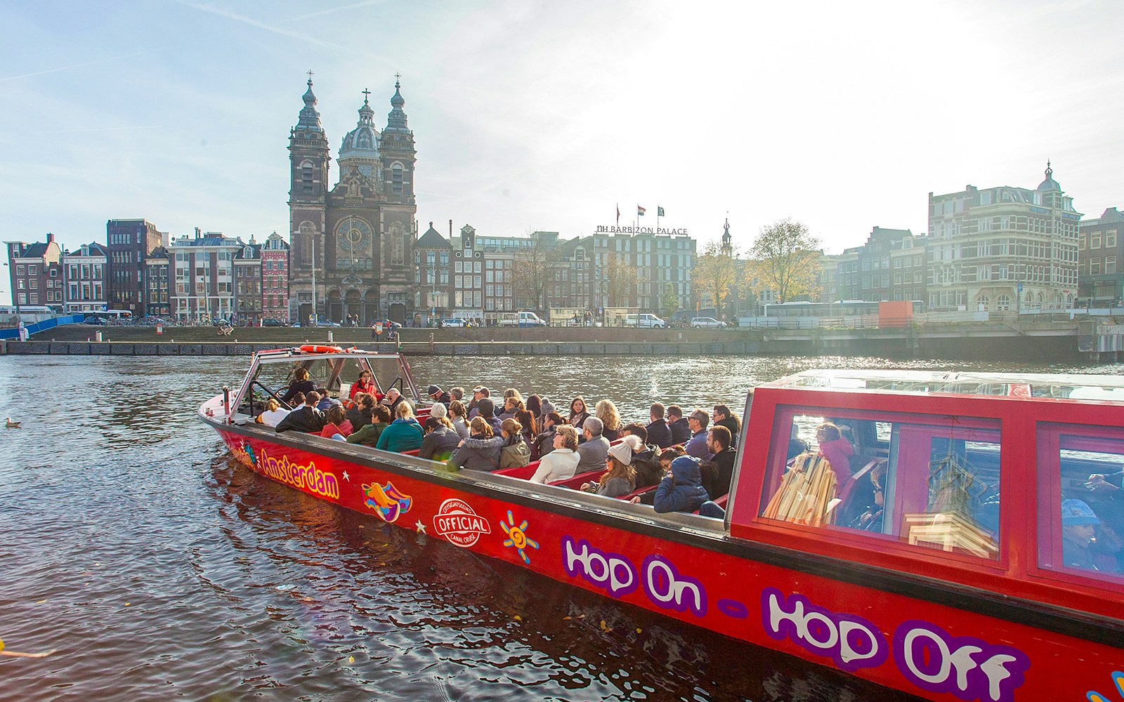 Amsterdam canal with hop-on hop-off tour boat passing historic buildings.