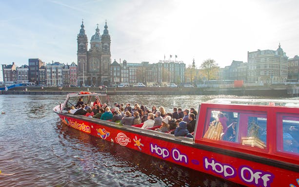 Hop on hop off boat tour with passengers on Amsterdam canal near historic buildings.