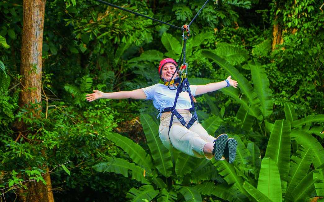 Tourist zip lining through lush forest at Hanuman World Zipline, Thailand.