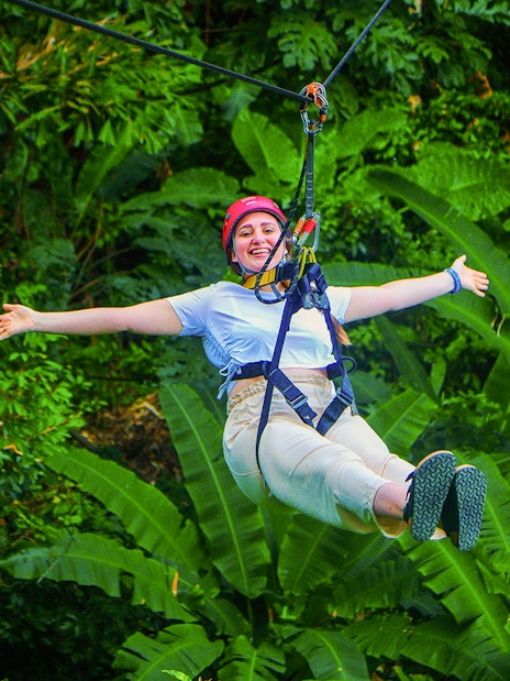 Tourist zip lining through lush forest at Hanuman World Zipline, Thailand.