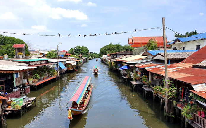 Longtail boat navigating Bangkok canal lined with traditional houses.