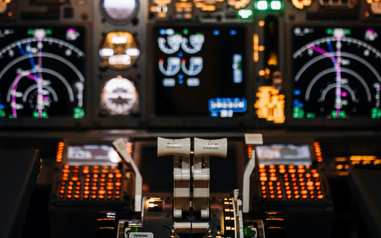Boeing 737NG simulator cockpit with illuminated control panels and throttle levers.