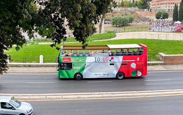 Open-top tour bus on Rome street with passengers enjoying city views.