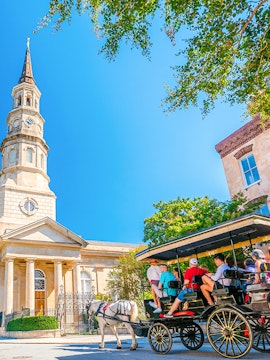 Horse-drawn carriage tour in front of historic church in downtown Charleston.