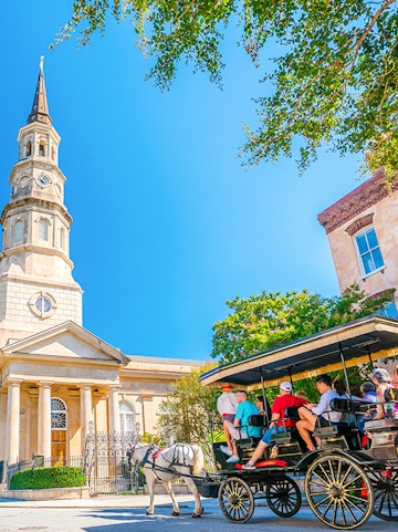 Horse-drawn carriage tour in front of historic church in downtown Charleston.