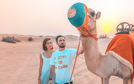 Couple with camel in Dubai desert during sunset, part of luxury family dinner and camel trekking experience.
