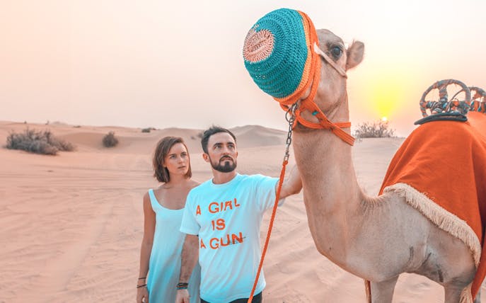 Couple with camel in Dubai desert during sunset, part of luxury family dinner and camel trekking experience.