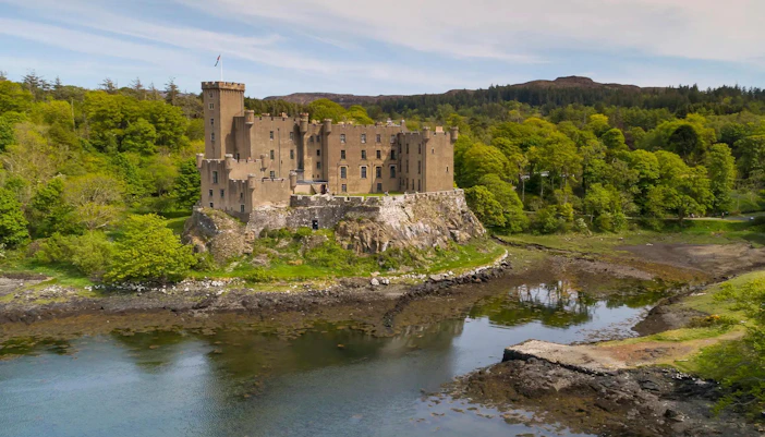 Dunvegan Castle on a rocky hill surrounded by lush greenery and water in Scotland.