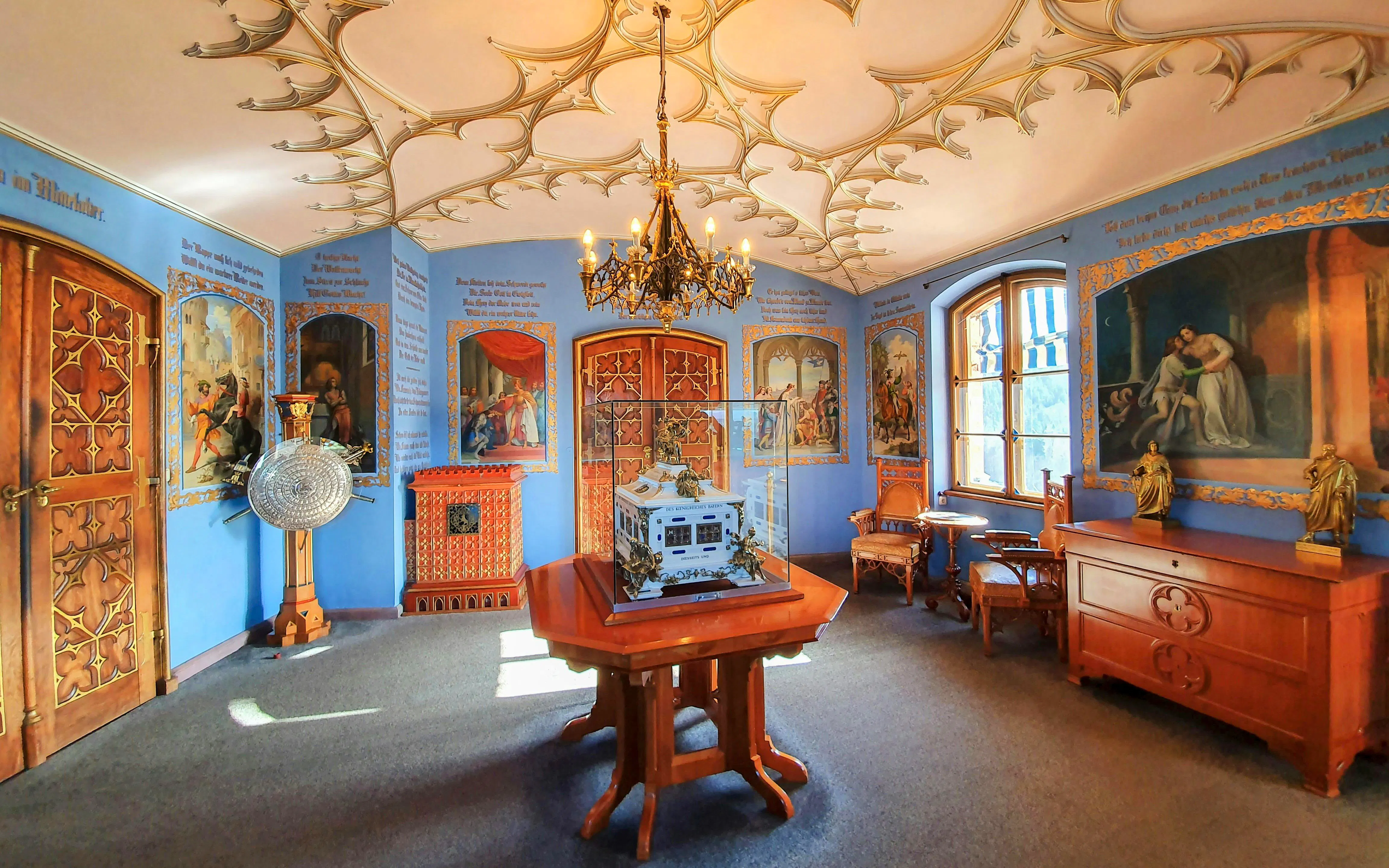 Interior room of Hohenschwangau Castle in Bavaria with ornate ceiling and historical paintings.