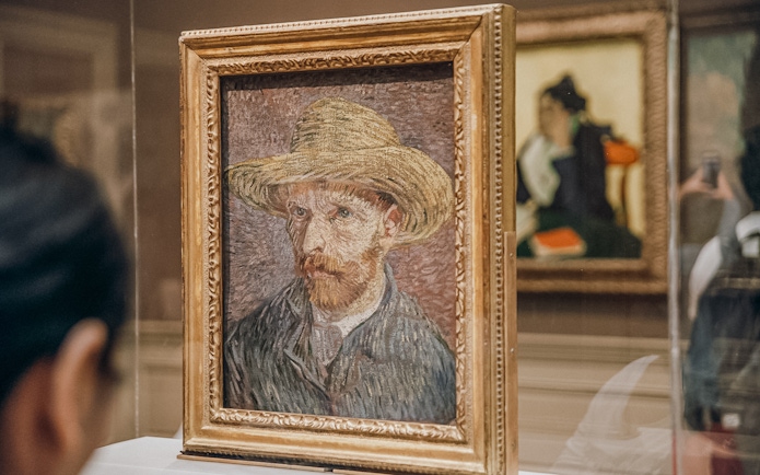 Van Gogh self-portrait with straw hat displayed in museum exhibit.