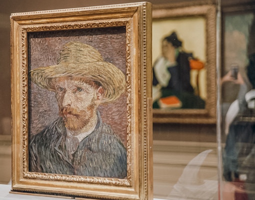 Van Gogh self-portrait with straw hat displayed in museum exhibit.