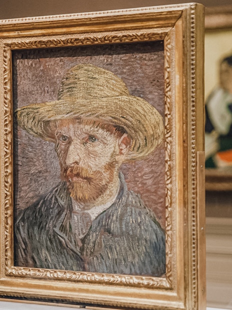 Van Gogh self-portrait with straw hat displayed in museum exhibit.