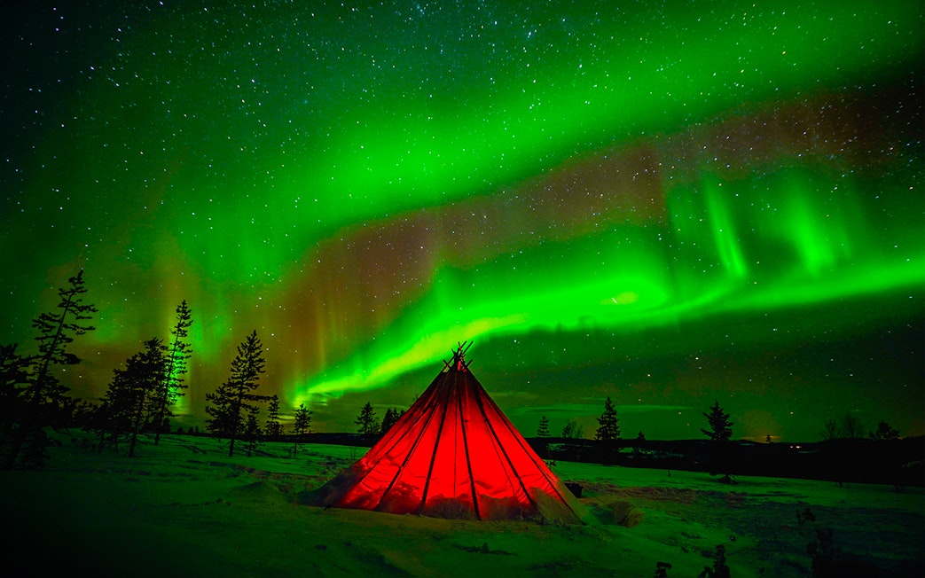 Northern Lights over a glowing tent in snowy Rovaniemi, Finland.