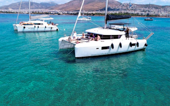 Lagoon 42 catamaran with people sailing in clear blue waters near a coastal city.