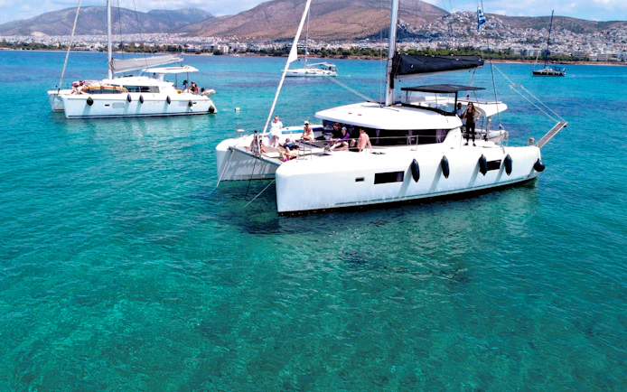 Lagoon 42 catamaran with people sailing in clear blue waters near a coastal city.