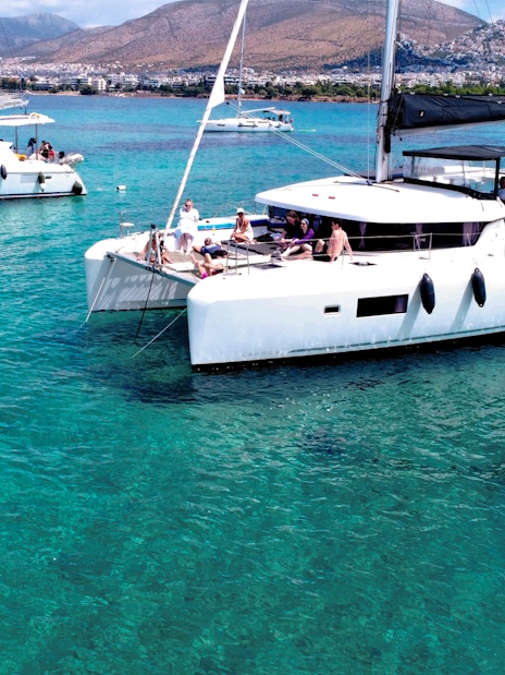 Lagoon 42 catamaran with people sailing in clear blue waters near a coastal city.