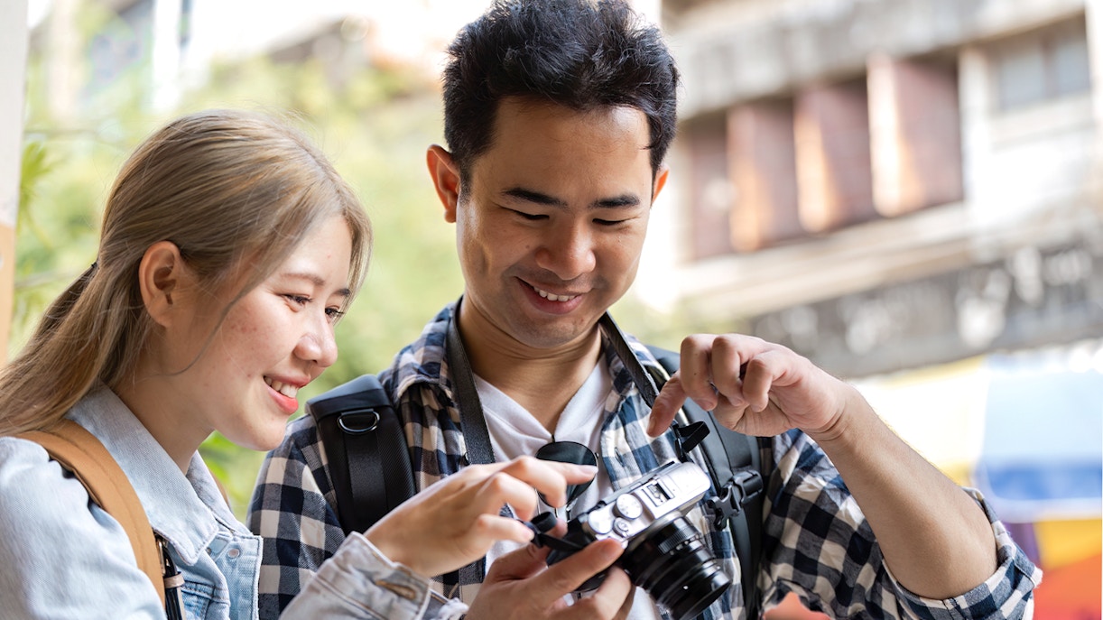 Man and woman posing with cameras in a scenic outdoor setting, capturing travel memories.