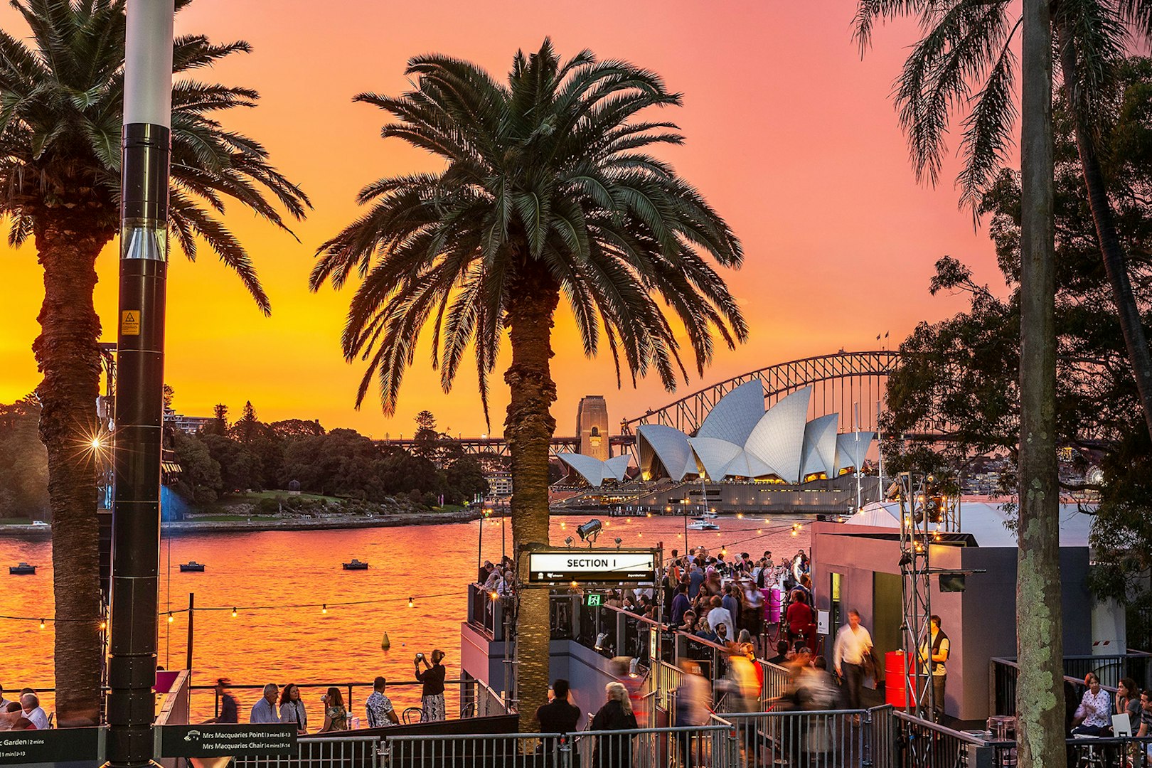 Sydney Harbour sunset with Opera House and Harbour Bridge, crowd gathering for West Side Story event.