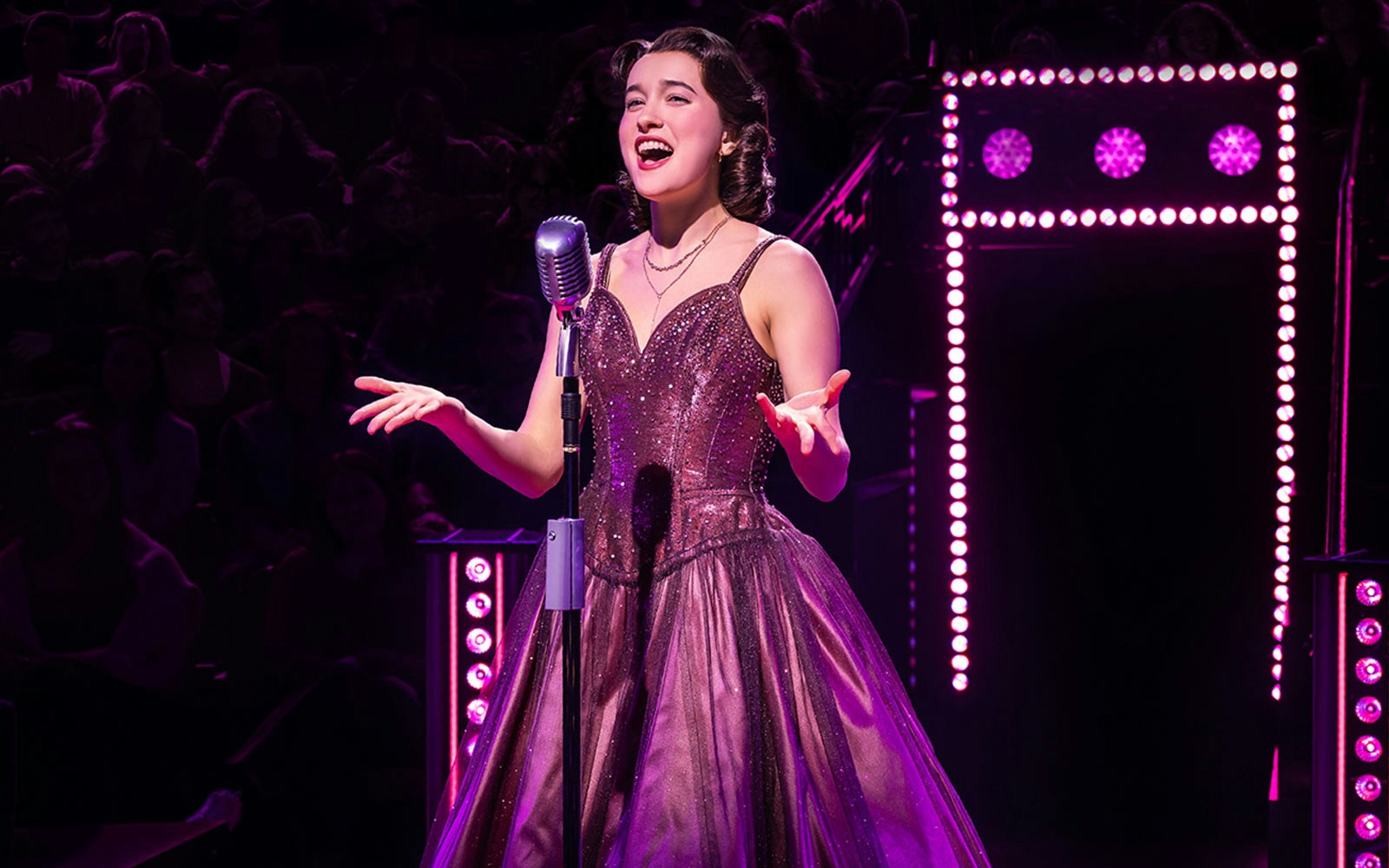 Singer performing on stage with vintage microphone, surrounded by purple lights.