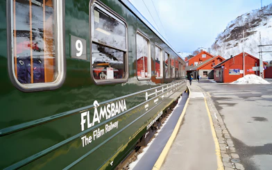 Flåm Railway train at snowy station with red buildings in Norway.