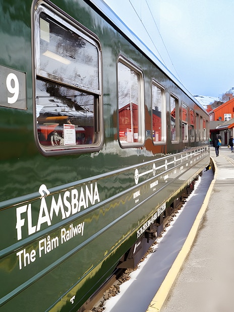 Flåm Railway train at snowy station with red buildings in Norway.