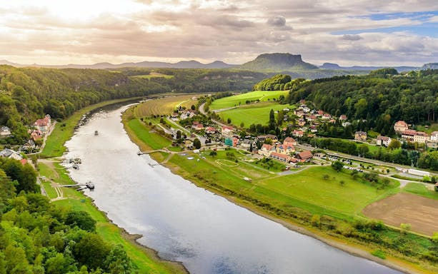 Aerial view of Elbe River and village in Saxon Switzerland, Germany, with lush greenery and distant hills.