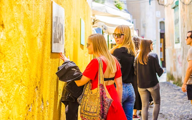 Woman viewing Camilla Watson's portraits on a yellow wall in Lisbon.