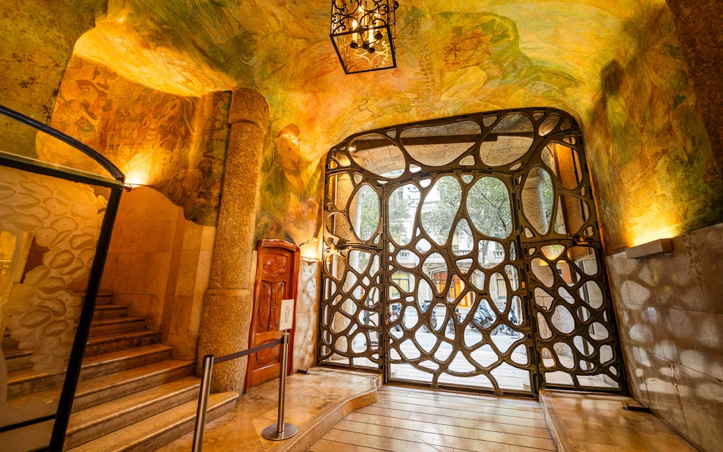 La Pedrera Casa Mila interior gate with ornate ironwork and colorful ceiling murals.