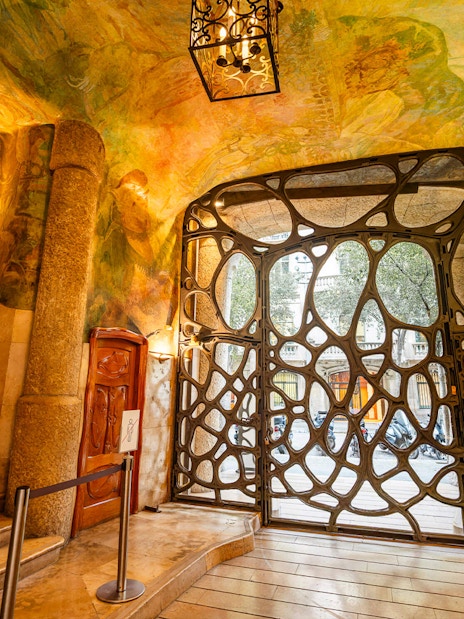 La Pedrera Casa Mila interior gate with ornate ironwork and colorful ceiling murals.