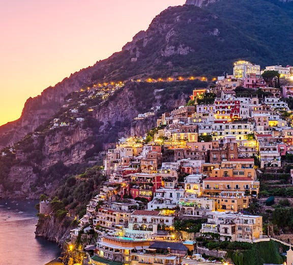 Positano hillside with colorful buildings at sunset, part of Rome to Positano tours.
