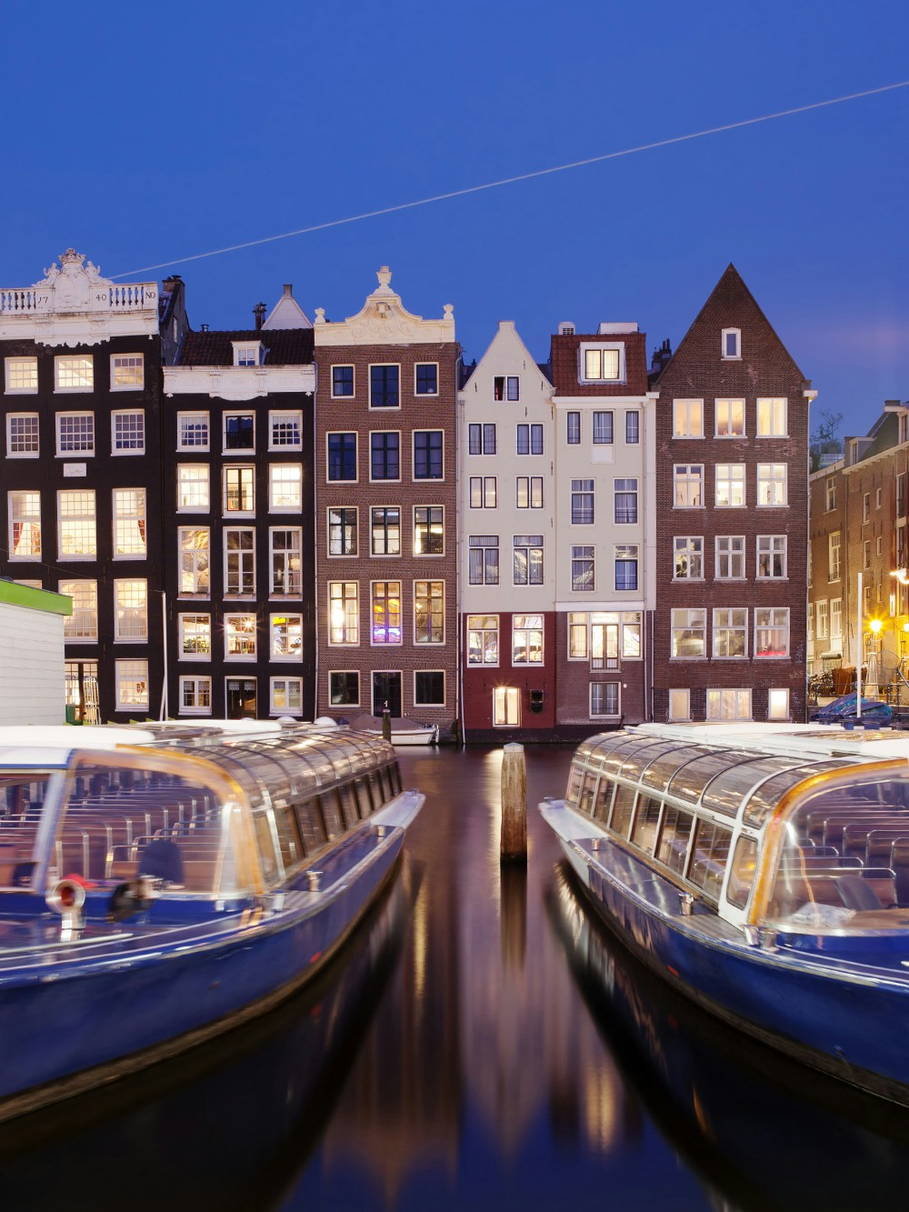 Canal boats docked in front of illuminated Amsterdam houses during a dinner cruise.