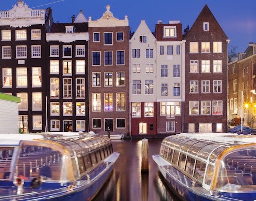 Canal boats docked in front of illuminated Amsterdam houses during a dinner cruise.