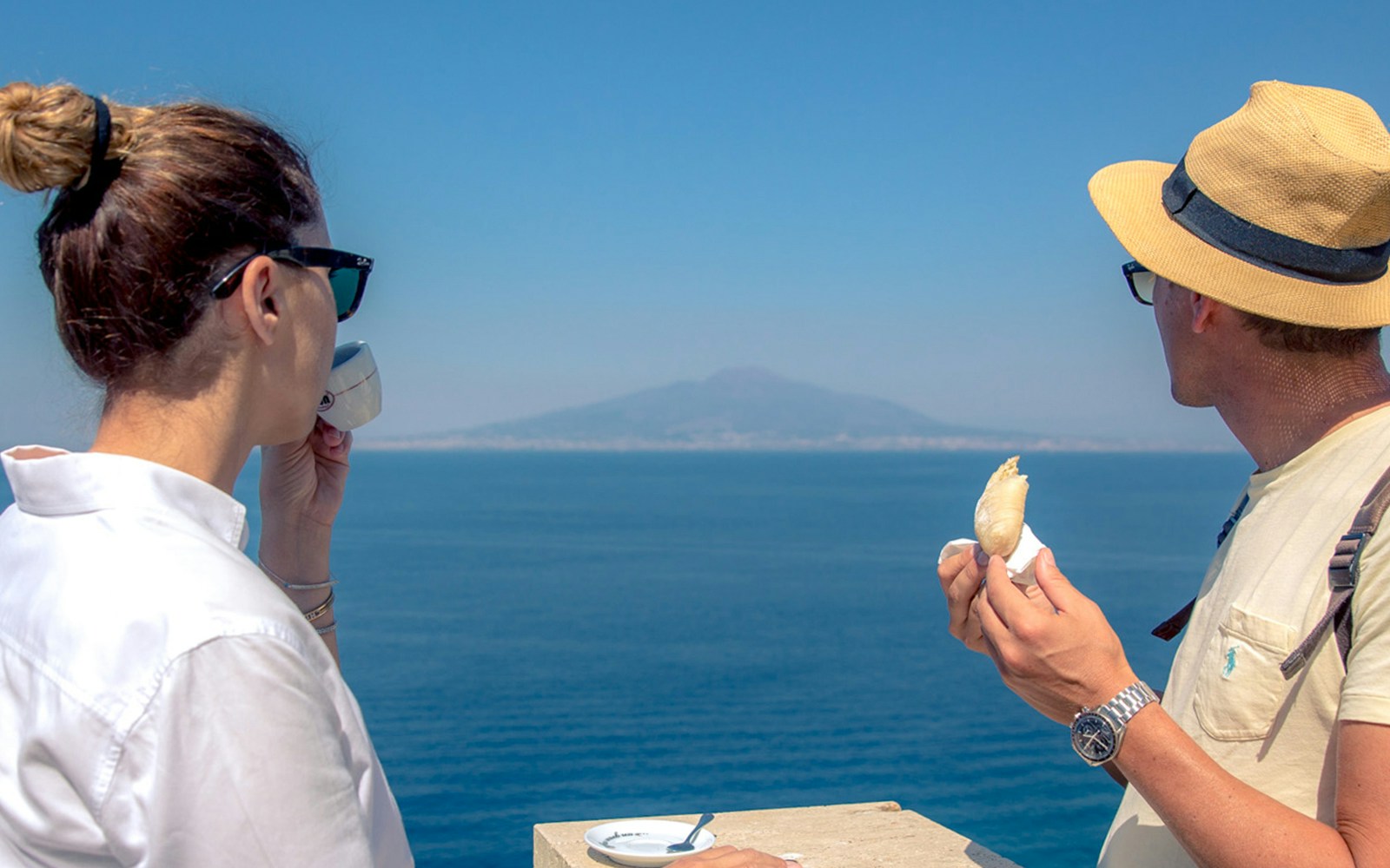 Tourists enjoying coffee and pastry with a view of Mount Vesuvius on a Sorrento walking tour.