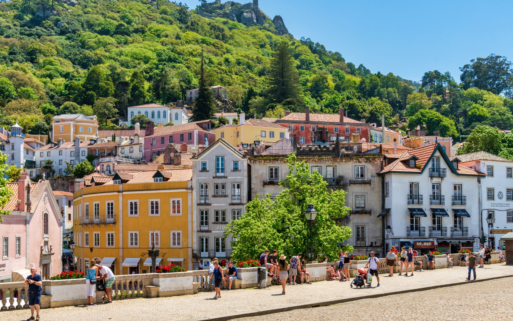 Colorful buildings and tourists in the town of Sintra, Portugal, with lush hills in the background.