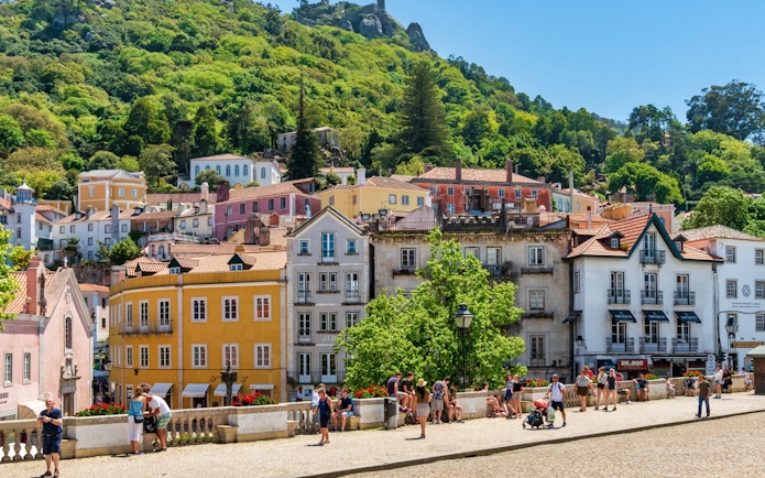 Colorful buildings and tourists in the town of Sintra, Portugal, with lush hills in the background.