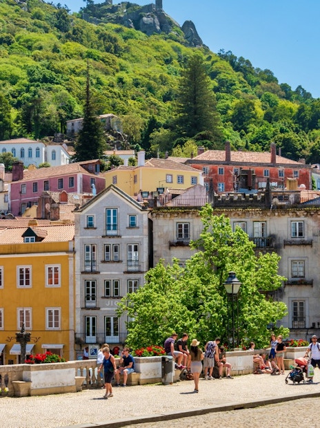 Colorful buildings and tourists in the town of Sintra, Portugal, with lush hills in the background.