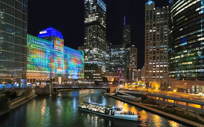 Dinner cruise boat on Chicago River with illuminated city skyline at night.