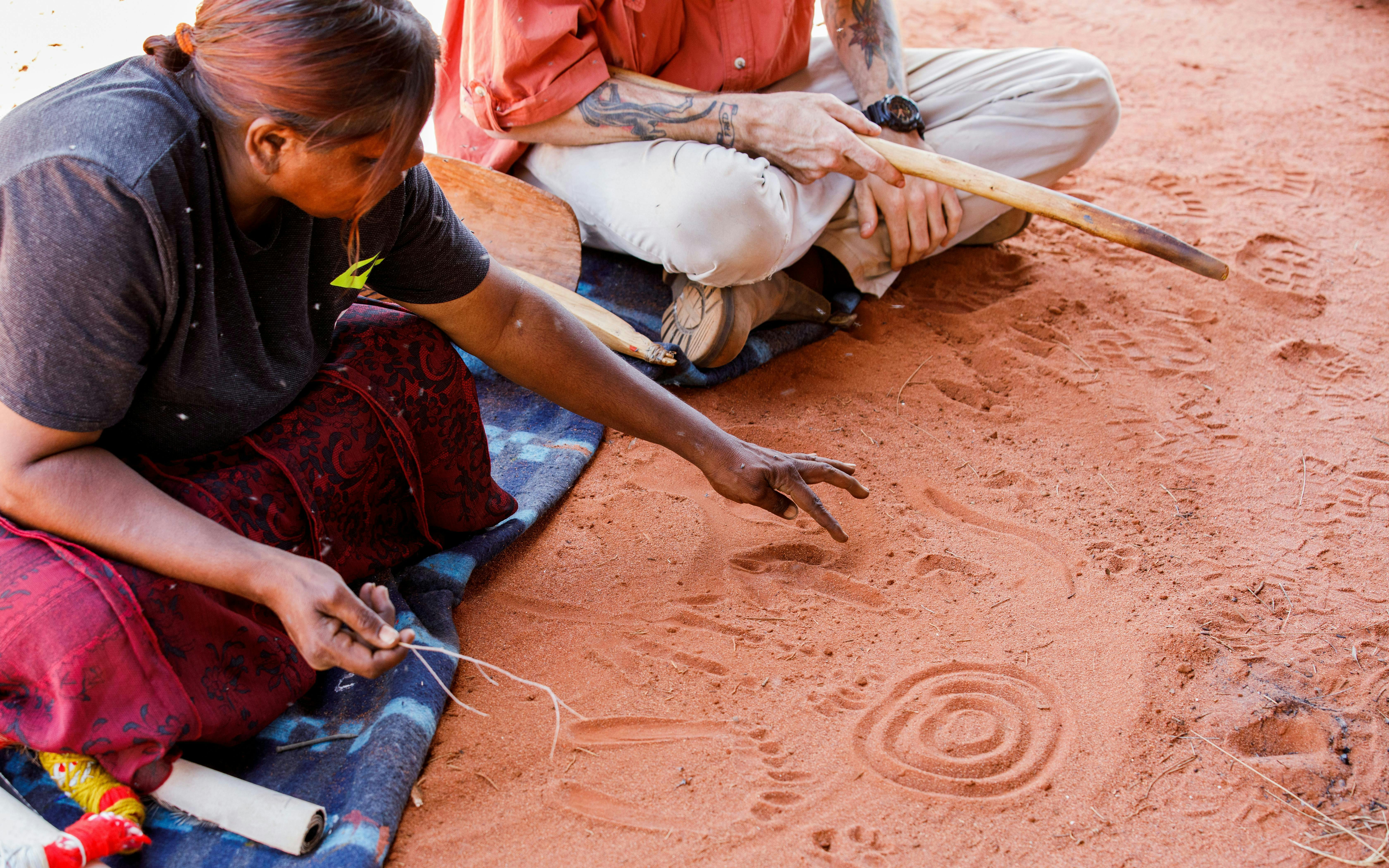 Aboriginal guide sharing stories and symbols in sand during Uluru sunrise tour.