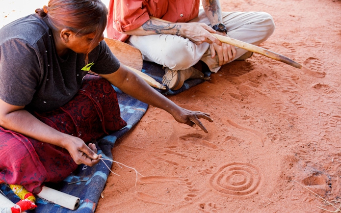 Aboriginal guide sharing stories and symbols in sand during Uluru sunrise tour.