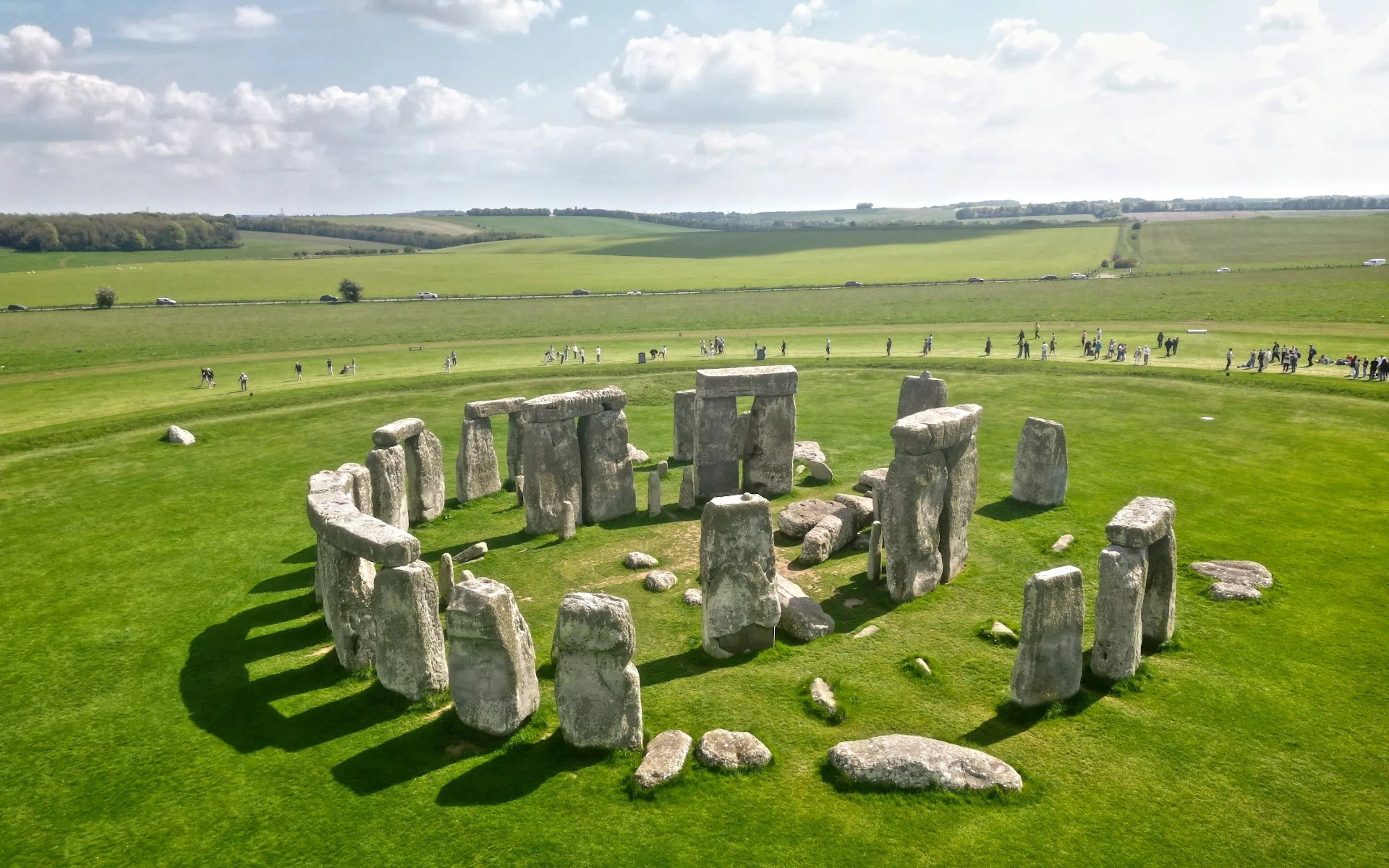 Stonehenge stone circle on a grassy plain with tourists in the background.
