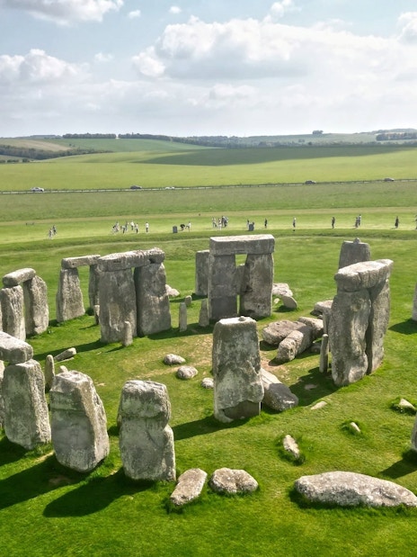 Stonehenge stone circle on a grassy plain with tourists in the background.