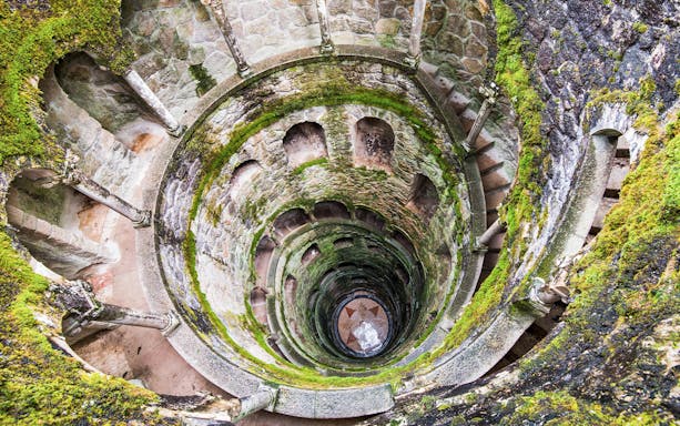Quinta da Regaleira's Initiation Well in Sintra, Portugal, with moss-covered spiral staircase.