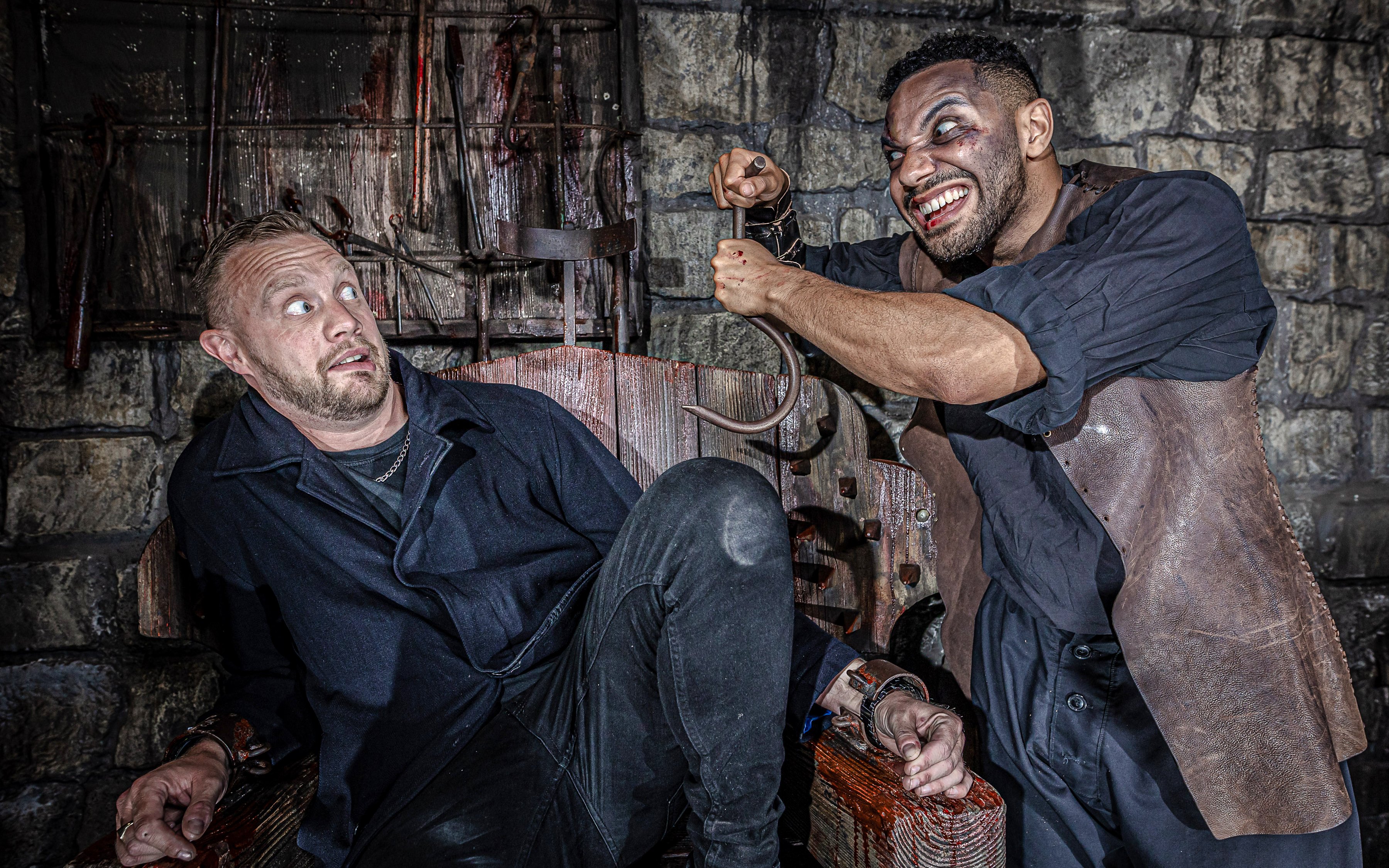 Man in distress in torture chamber at York Dungeon with actor holding hook.