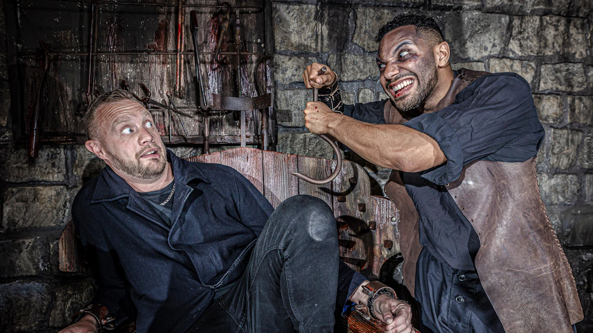 Man in distress in torture chamber at York Dungeon with actor holding hook.