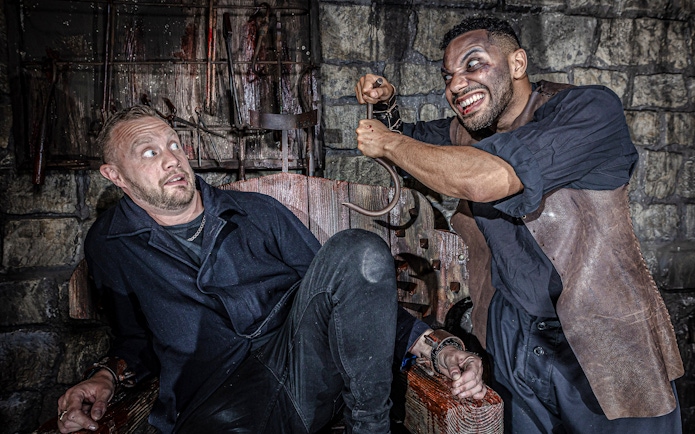 Man in distress in torture chamber at York Dungeon with actor holding hook.