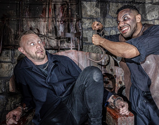 Man in distress in torture chamber at York Dungeon with actor holding hook.