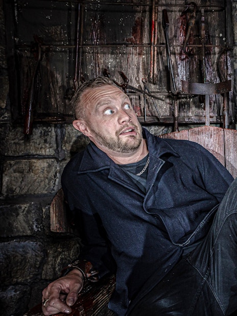 Man in distress in torture chamber at York Dungeon with actor holding hook.